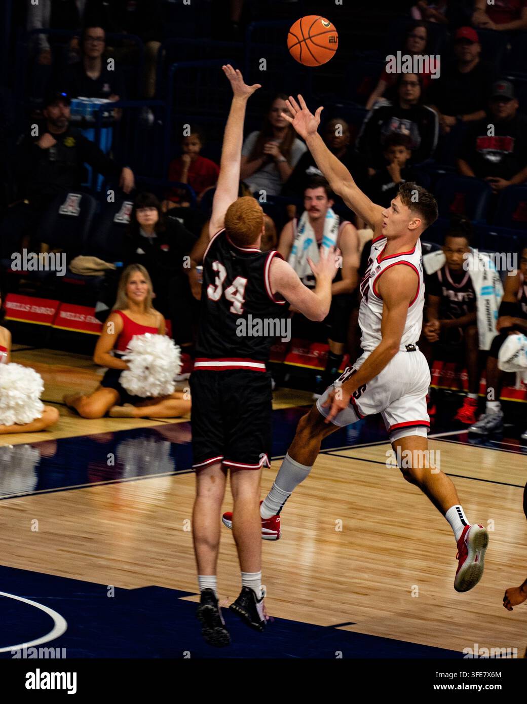 Tucson, Arizona - November 2022: Ein Basketballspieler der Arizona Wildcats springt zu einem Wurf, während ein Verteidiger ihn blockiert, mit Cheerleadern, die auf der Bank sitzen Stockfoto