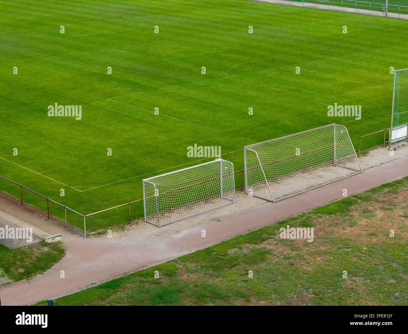 Leeres Fußballfeld mit leuchtend grünem Rasen, weißen Markierungen und mobilen Toren neben gepflastertem Gehweg an einer Schule oder im Stadion eines Sportvereins. Ruhiges Training Stockfoto