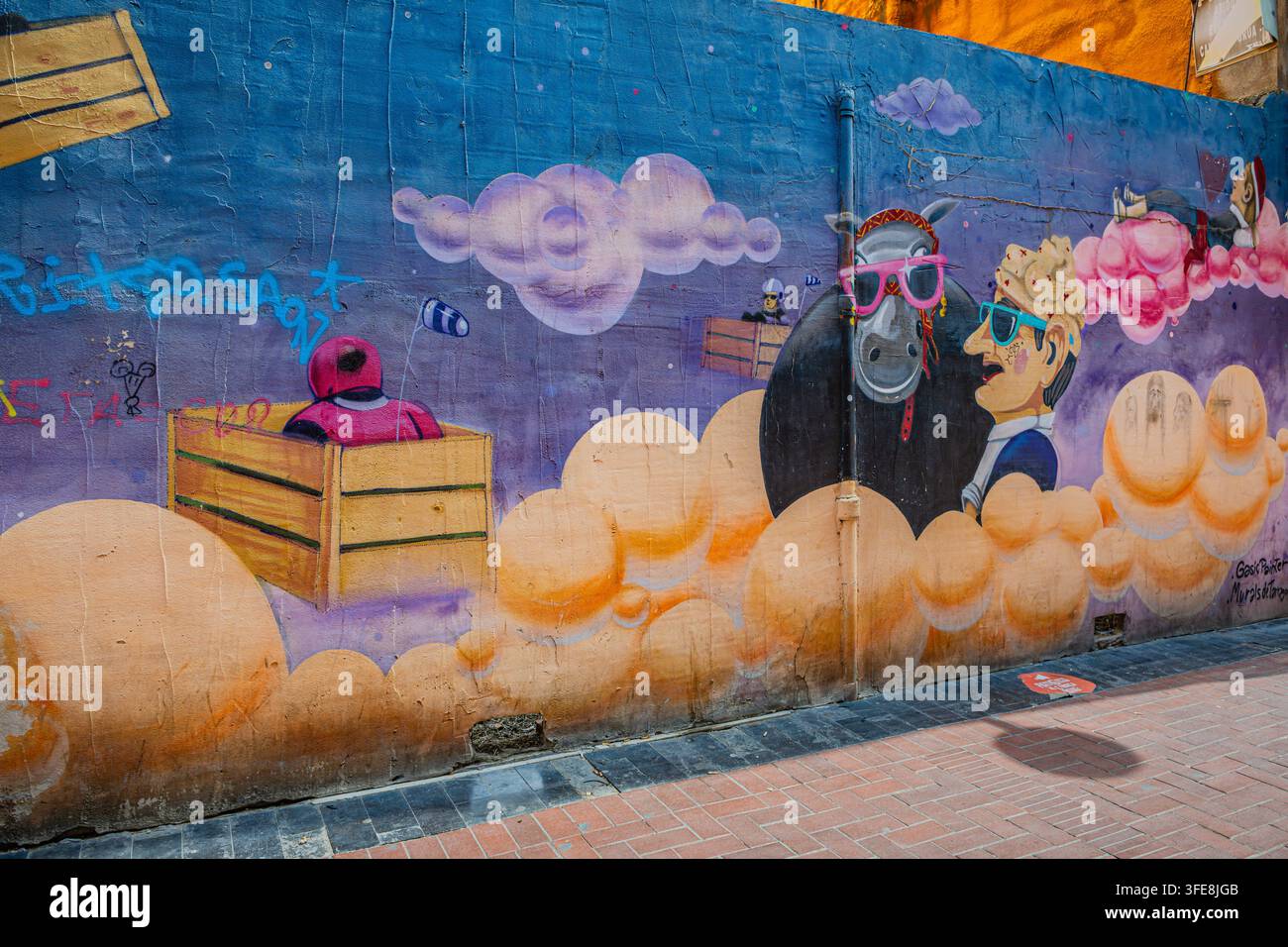 Farbenfrohes Straßenkunst-Mural zeigt verspielte Figuren, Wolken und Holzkisten an einer Außenwand in Reus Stockfoto