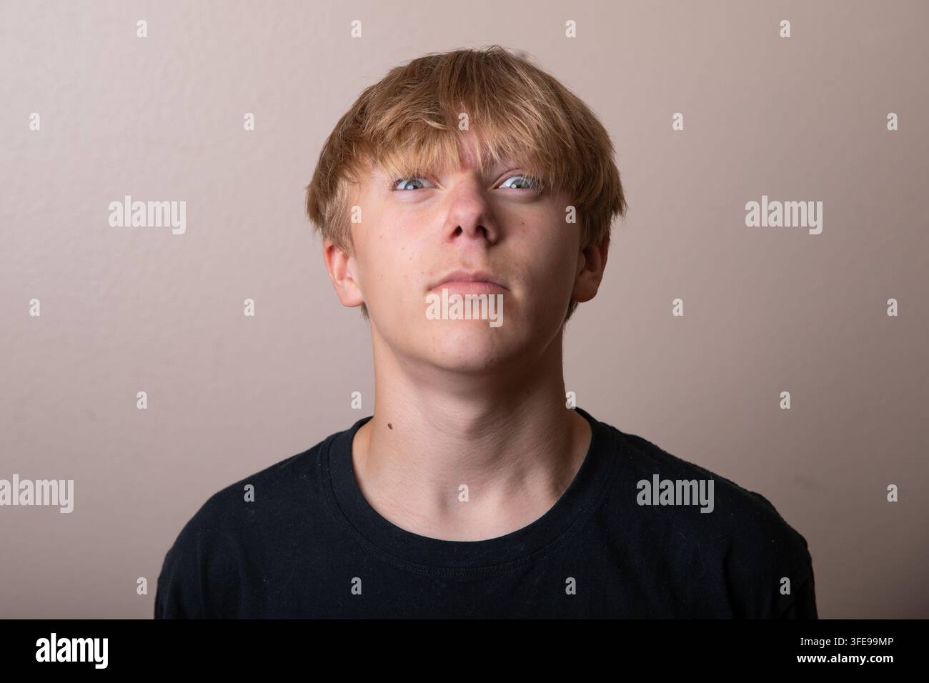 Ein junger Mann mit kahlgeschorenem Kopf und einem schwarzen Hemd schaut in die Kamera Stockfoto