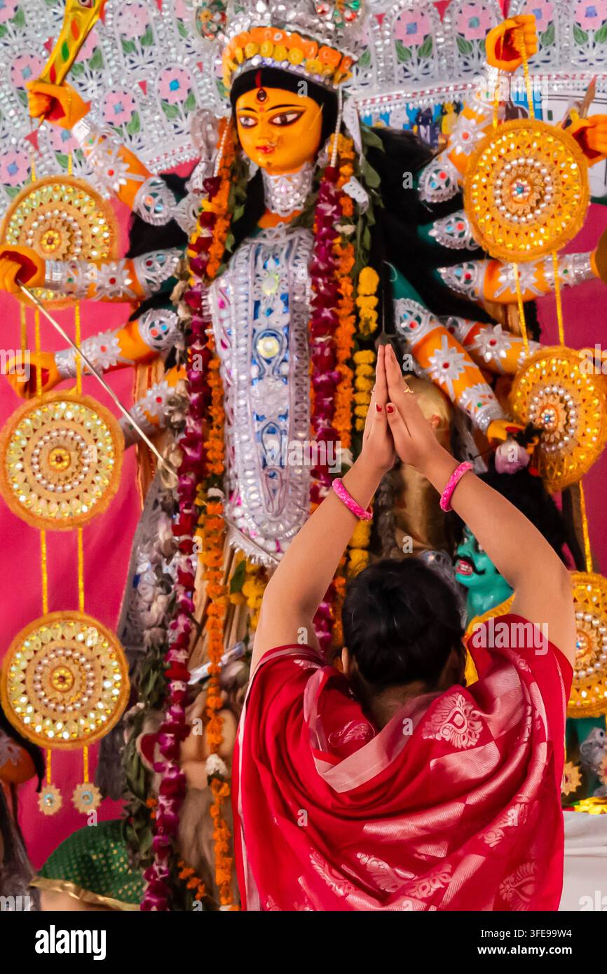 Frauenanhängerin, die Gebete vor einem verschwommenen, verzierten Durga-Göttinnenidol während Durga Puja darbringt Stockfoto