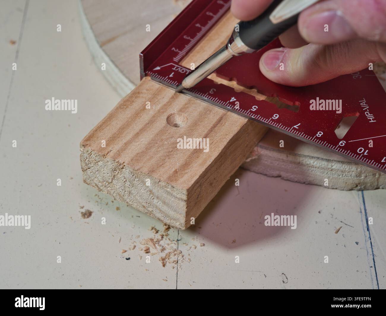 Speed Square auf Holz mit Spänen - Ein rotes Aluminium-Speed Square ist auf einem Stück hellfarbigen Holzes mit einem gebohrten Loch und Holzspänen positioniert Stockfoto