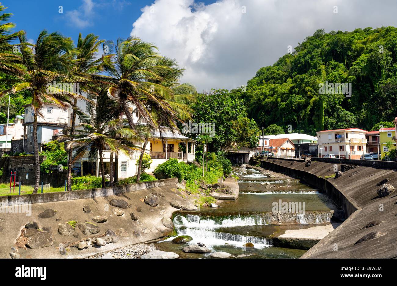 Ein wunderschöner Blick auf den Grand Riviere-Fluss mit kleinen Wasserfällen, die durch die tropische Stadt Grand Riviere in Martinique fließen, umgeben von Palmen und üppigen Hügeln Stockfoto