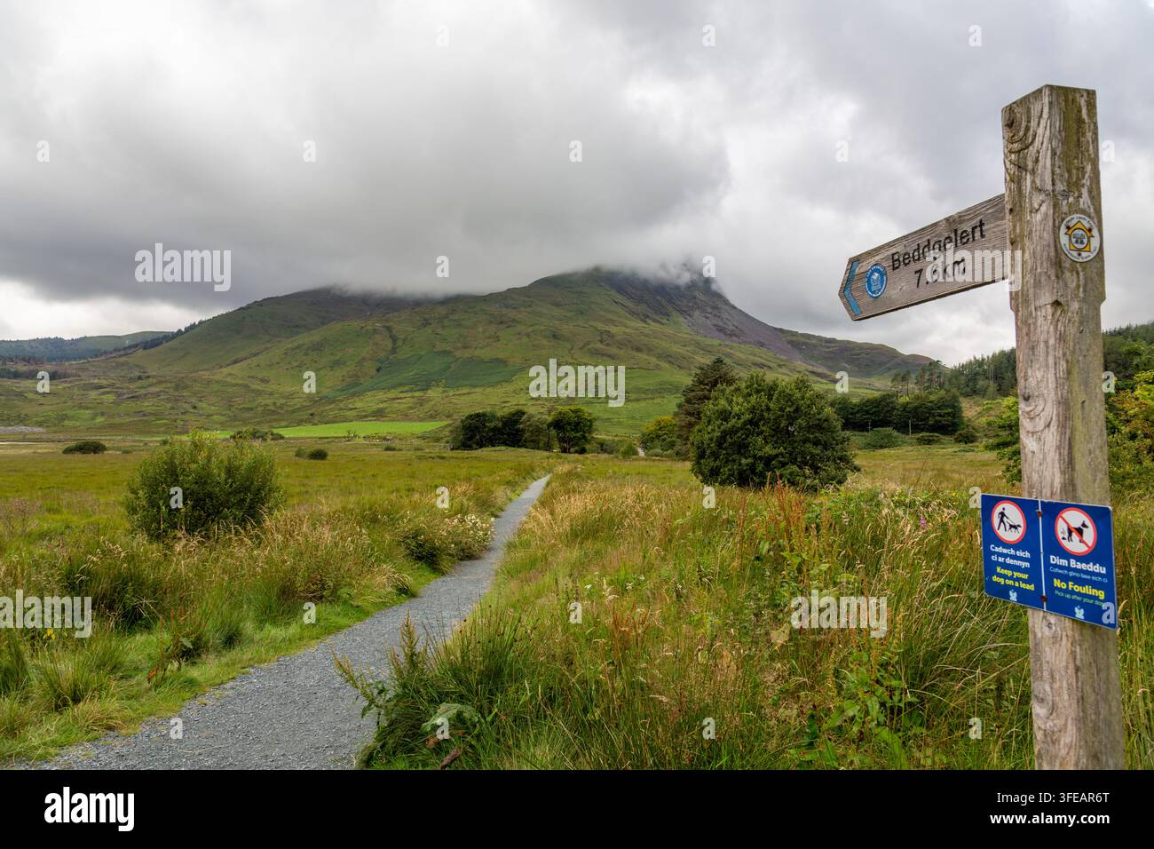Ein Wegweiser zeigt an einem bewölkten Tag den Weg nach Beddgelert mit Y Garn und Mynyd Drws Y Coed im Hintergrund Stockfoto