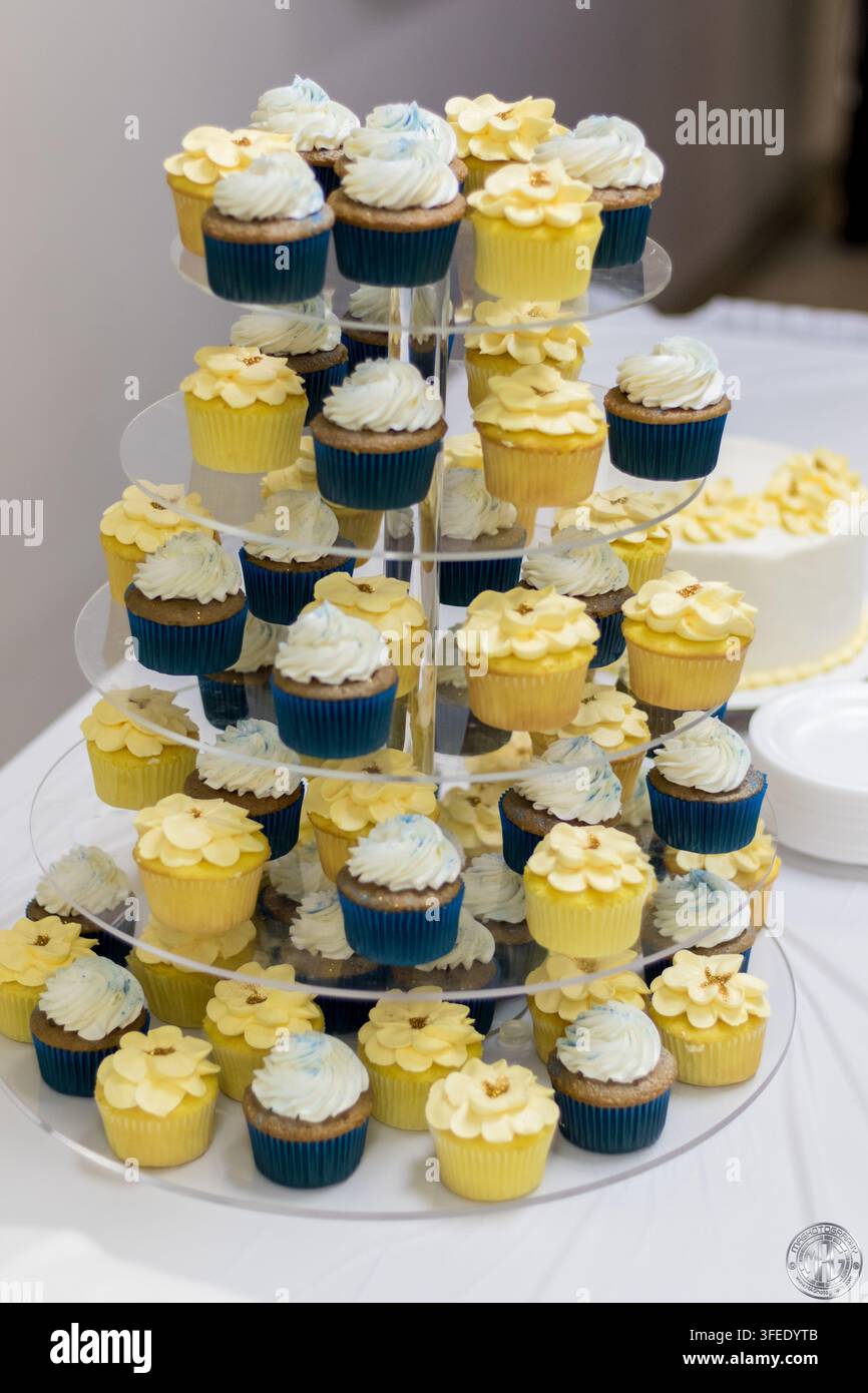 Ein mehrstufiger klarer Acrylständer gefüllt mit gelben und blauen dekorierten Cupcakes bei einem Hochzeitsempfang oder einer Party-Desserttischgestaltung. Stockfoto