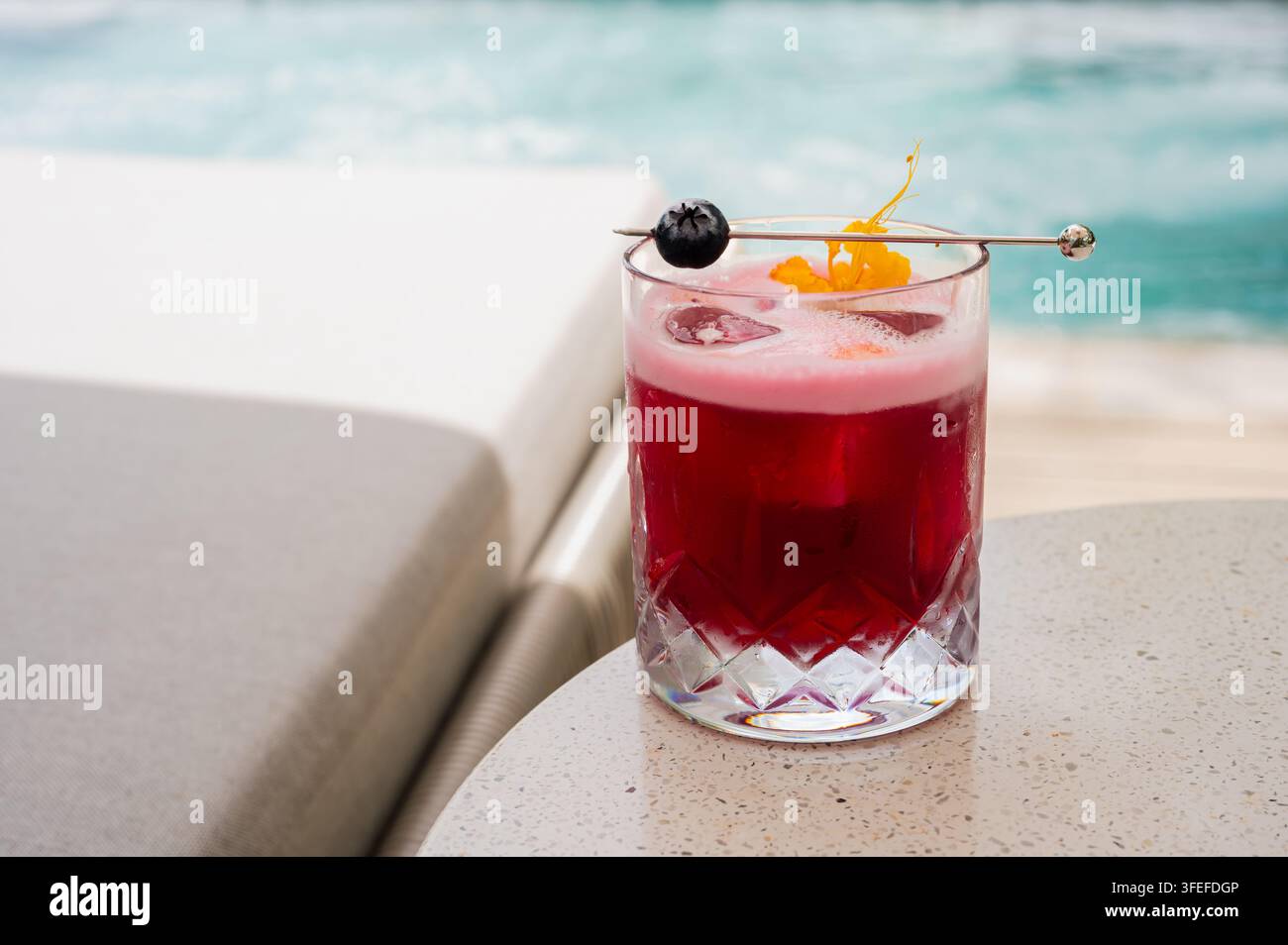Roter Cocktail mit Obstgarnitur auf einem Tisch am Pool. Stockfoto