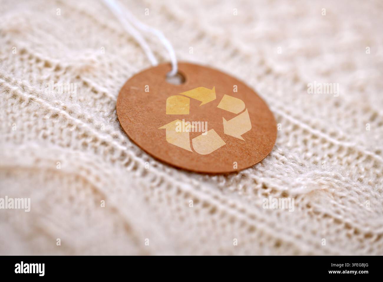 Braunes Bastelpapier-Kleidungsetikett mit Recyclingsymbol auf weißem Strickpullover Stockfoto