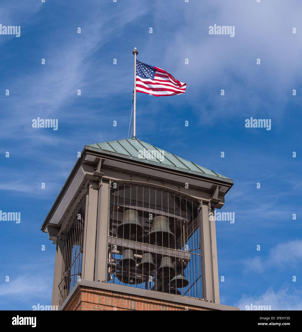 Amerikanische Flagge weht über einem historischen Glockenturm mit sichtbaren Glocken und blauem Himmel, zeigt Patriotismus, bürgerliches Erbe und nationalen Stolz. Stockfoto