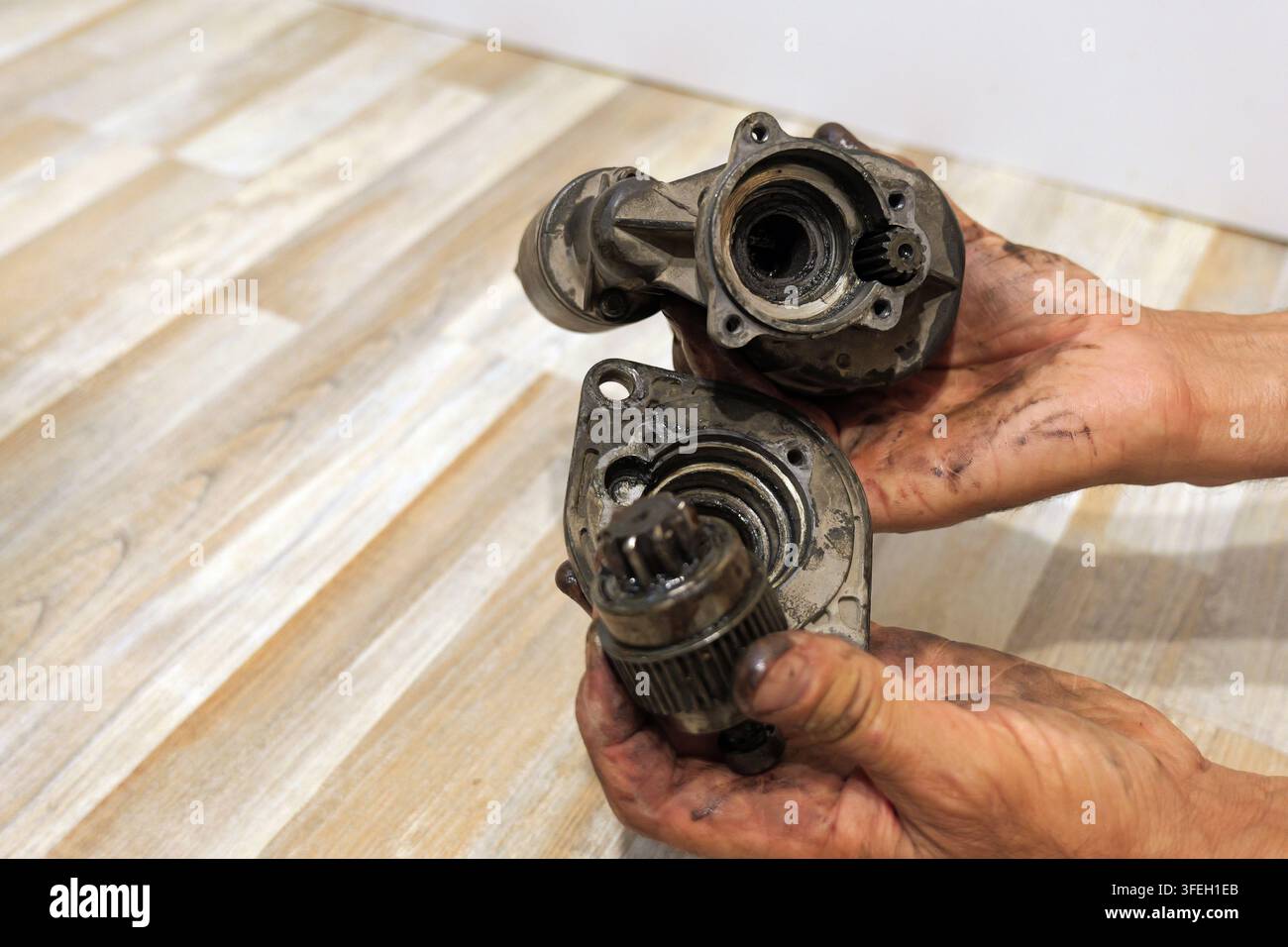 Mechanicsche Hände, mit Fett und Öl verschmiert, zerlegen einen defekten Auto-Startermotor zur Reparatur, wobei die internen Komponenten und das abgenutzte Zahnrad sichtbar sind Stockfoto