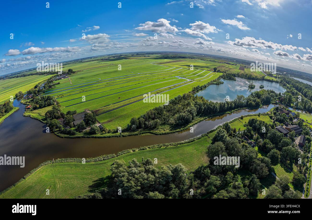 Die grünen Felder und gewundenen Wasserwege von Gelderswoude werden aus einer Höhe von 120 Metern eingefangen. Dieser weitläufige Blick zeigt die lebendige grüne Landschaft von Zoeterwoude und enthüllt die natürliche Schönheit von Südholland unter einem klaren blauen Himmel. Stockfoto