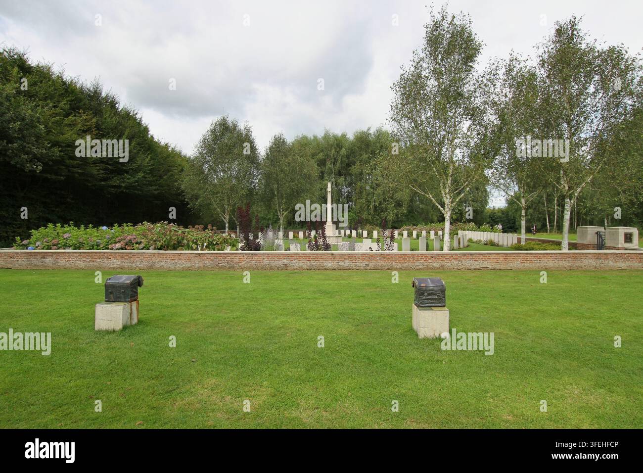 Das weiße steinerne Kreuz der Opferung steht zwischen Reihen von Grabsteinen hinter einer niedrigen Backsteinmauer auf einem Commonwealth-Militärfriedhof in Belgien. Stockfoto