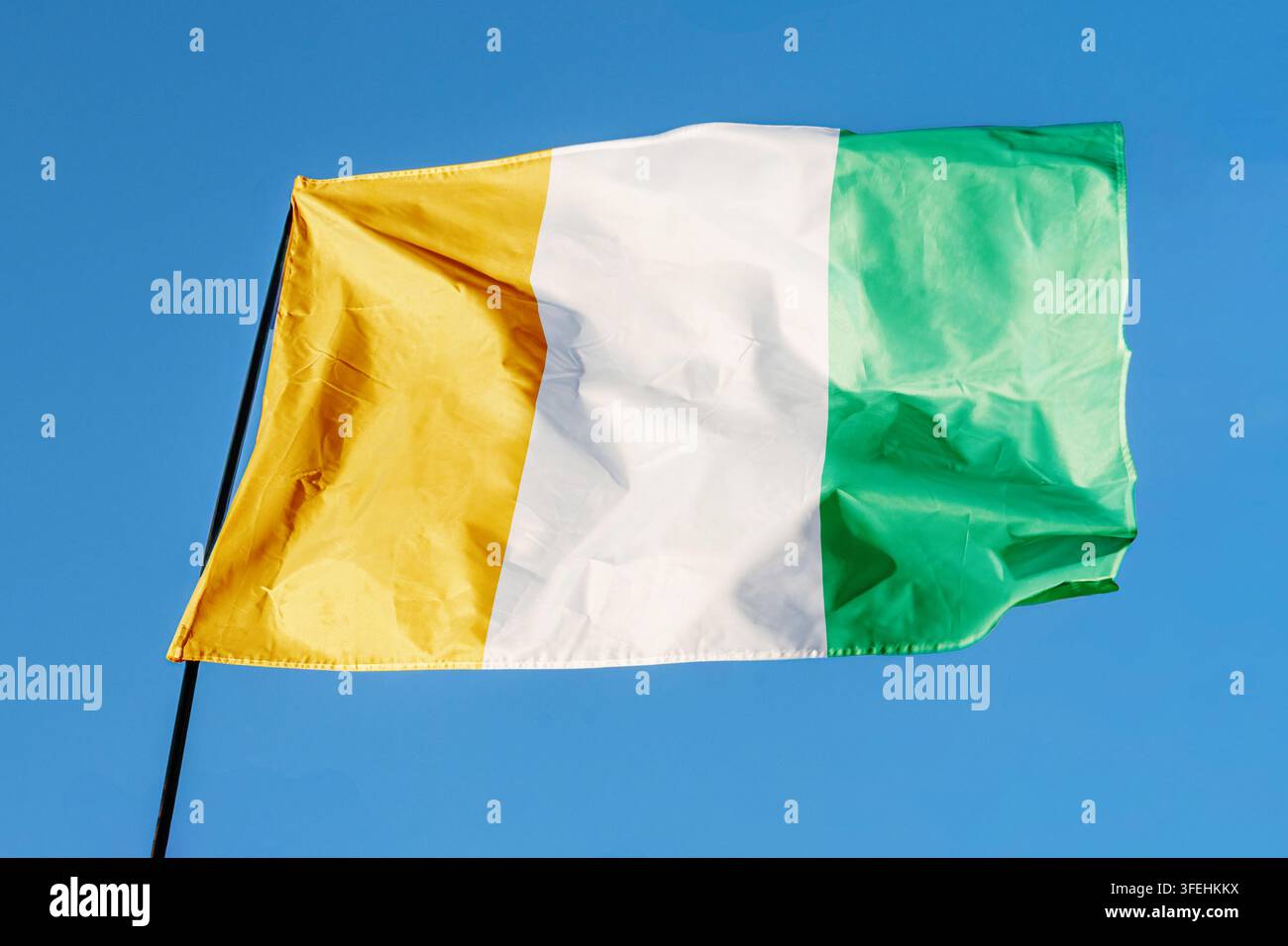 Flagge der Elfenbeinküste. Fahne weht im Wind vor einem klaren blauen Himmel, flattert an einer Fahnenstange im Freien. Helle Sonnentage, Stofftextur, Außenbereich Stockfoto