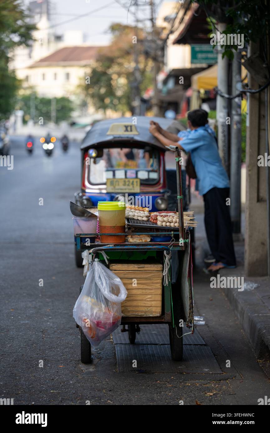 Bangkok, Thailand, 29. Januar 2026. Ein mit gegrillten Fleischspießen beladener Handwagen steht neben einem Tuk-Tuk auf einer Stadtstraße. Stockfoto
