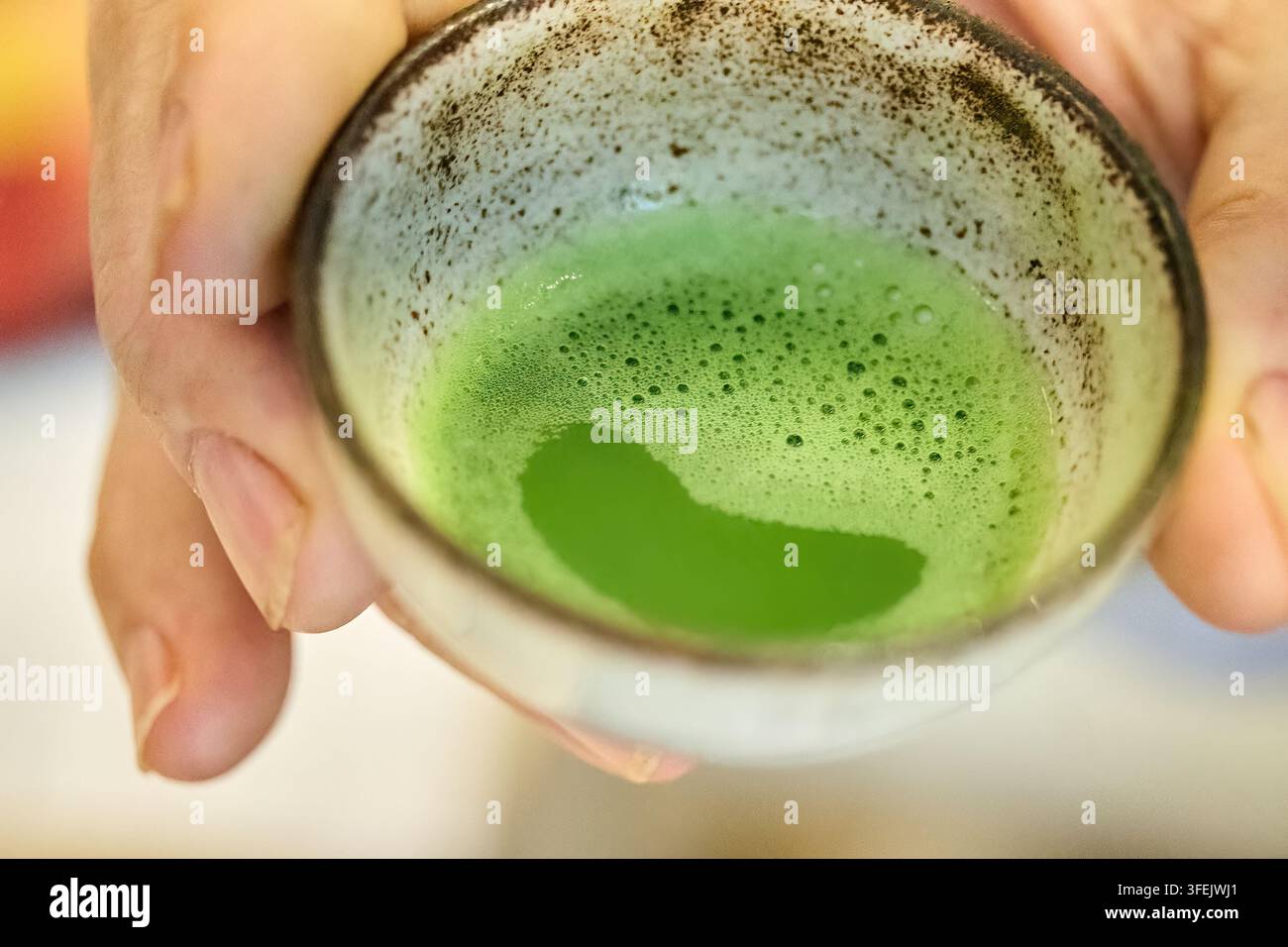 Hände, die eine traditionelle Keramiktasse mit Matcha-Tee halten Stockfoto