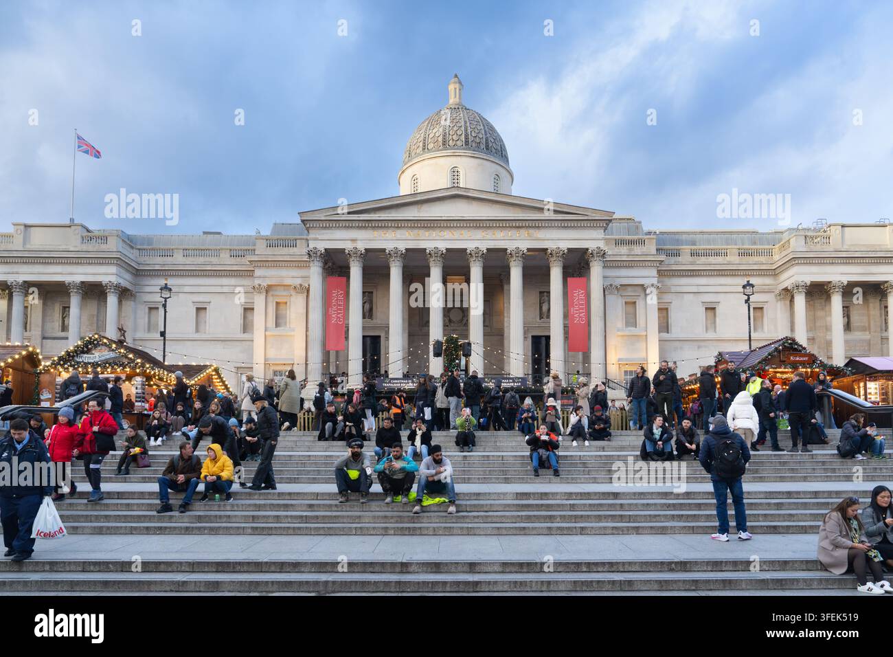 Touristen und Einheimische entspannen sich auf den Stufen der Nationalgalerie am Trafalgar Square in London und genießen einen festlichen Weihnachtsmarkt. Stockfoto