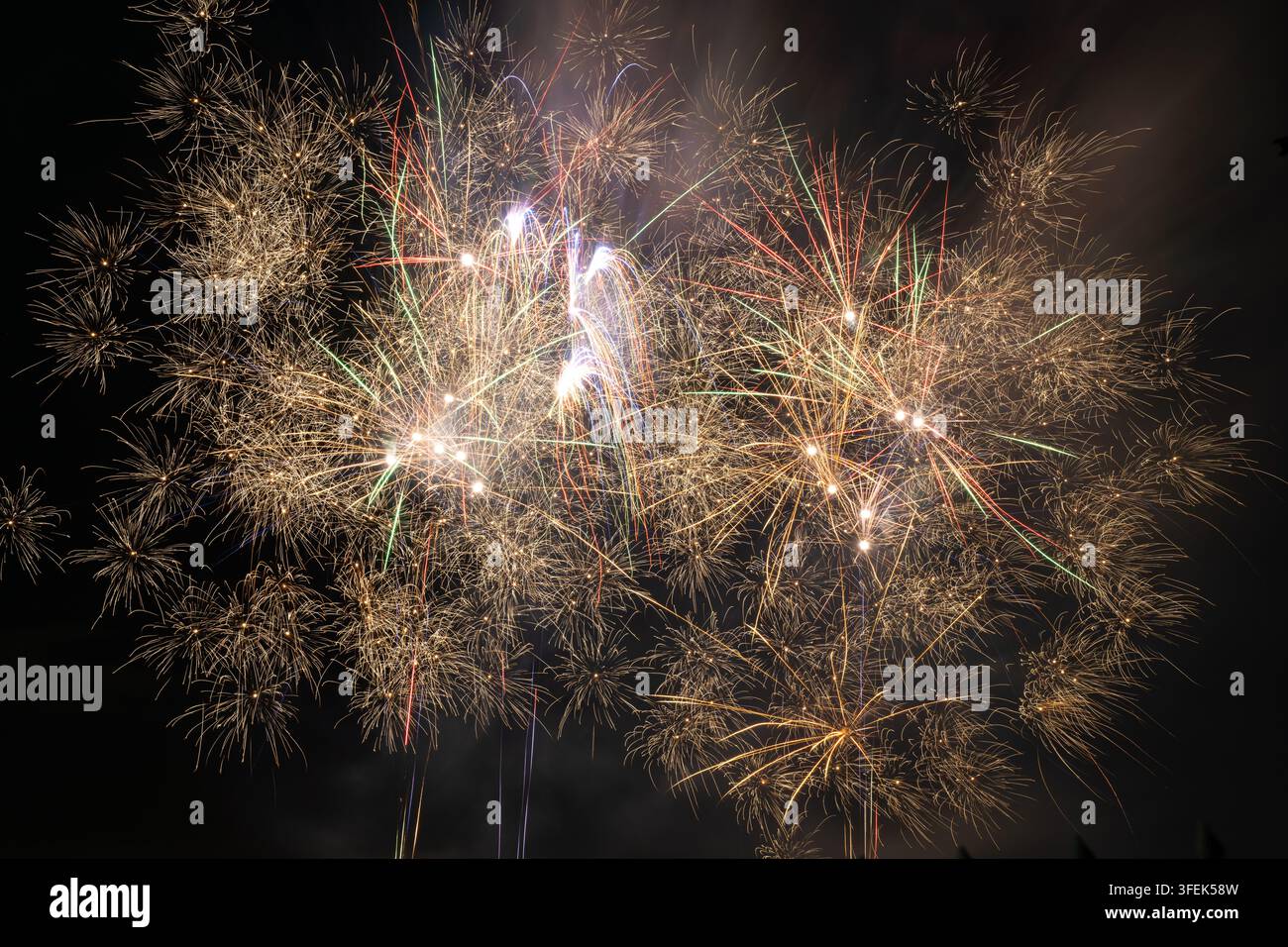 Lebendige Feuerwerke erleuchten den dunklen Nachthimmel während einer Feier und explodieren in brillanten goldenen und farbigen Mustern. Stockfoto