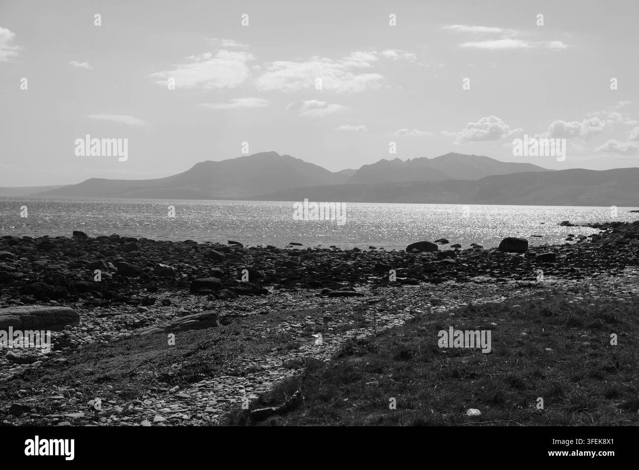 Eine Schwarz-Weiß-Landschaft zeigt eine felsige Küste, die über das Wasser zu den fernen Berggipfeln der Isle of Arran in Schottland blickt Stockfoto