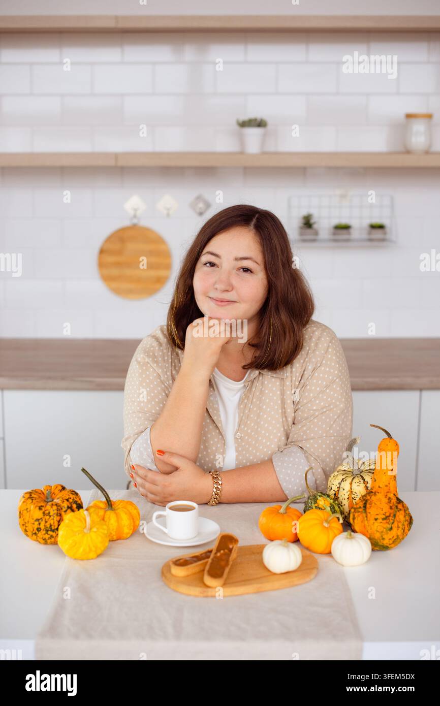 Frau genießt eine herbstliche Kaffeepause mit Kürbisdesserts und dekorativen Mini-Kürbissen in der Küche Stockfoto