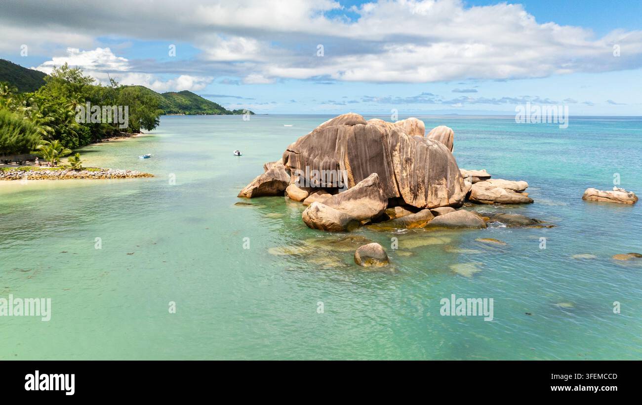 Massive Granitblöcke liegen in ruhigen türkisfarbenen Gewässern nahe der üppigen Küste. Praslin, Seychellen. Stockfoto