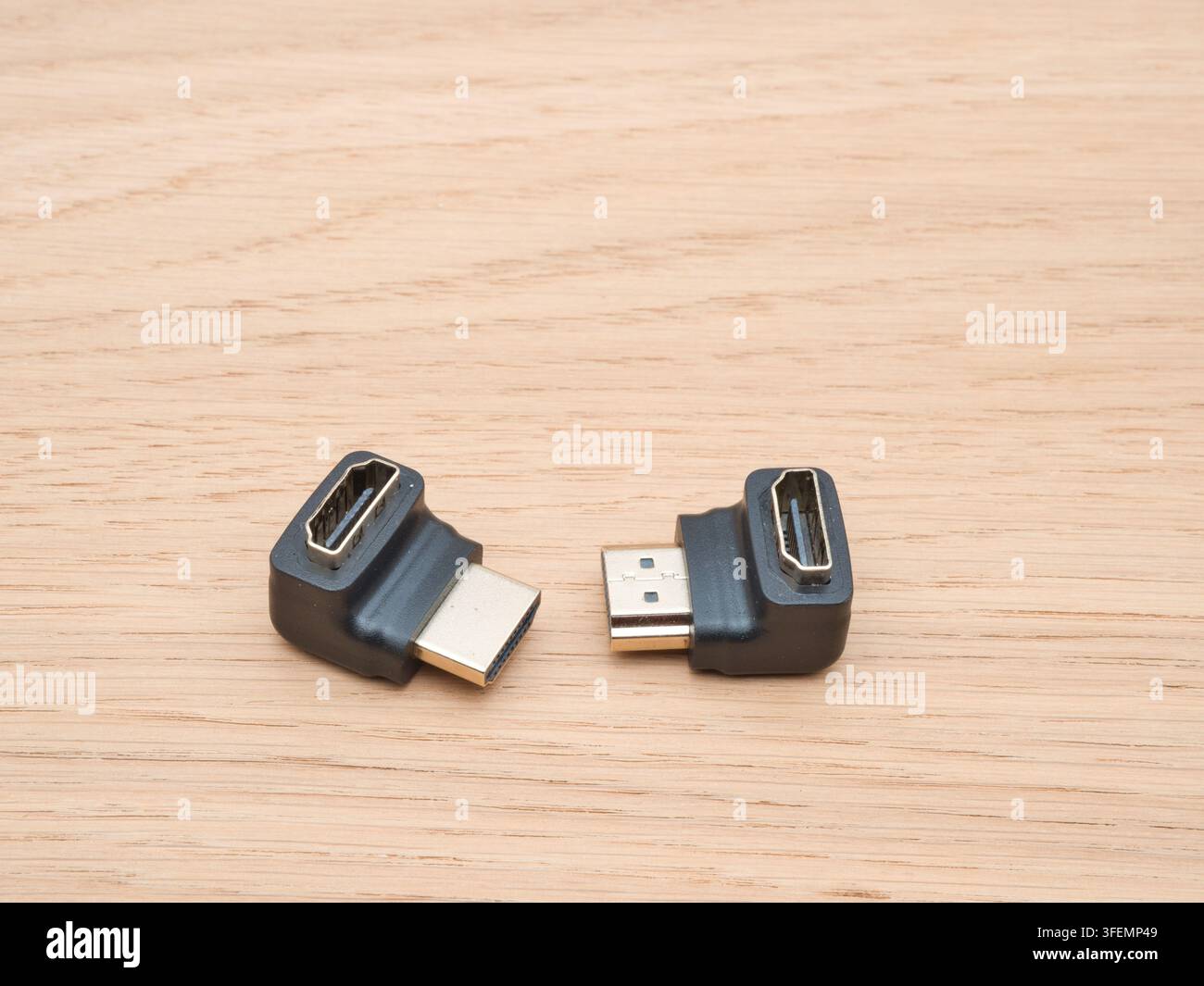 Rechteckige HDMI-Adapter auf Holz – Zwei L-förmige HDMI-Adapter mit vergoldeten Steckern werden auf einer hellen Holzoberfläche angezeigt, bereit für Elektron Stockfoto
