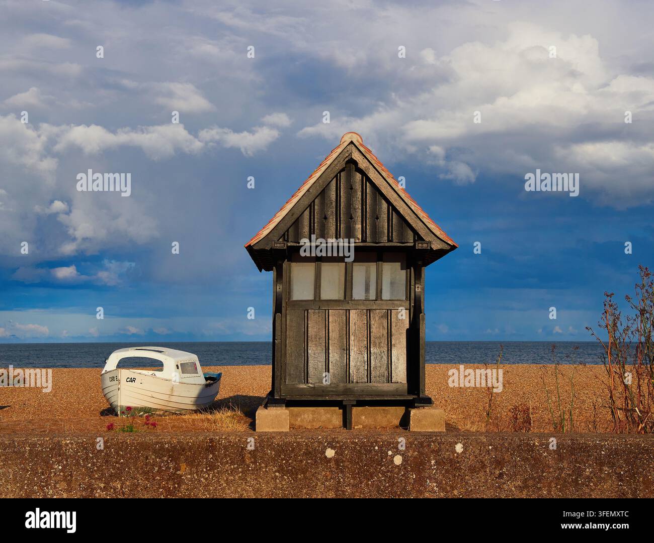 Verwitterte Strandhütte und kleines Boot auf Kiesufer unter dramatischem bewölktem Himmel am Meer Stockfoto