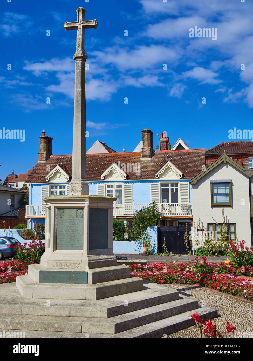 Steinernes Kriegsdenkmal-Kreuz auf dem Platz einer Küstenstadt mit Häusern und Blumenbeeten unter blauem Himmel Stockfoto