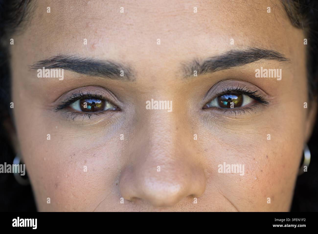 Afroamerikanische Frau zeigt dezentes Augen-Make-up im Studio-Porträt mit silbernen Kreolen Stockfoto