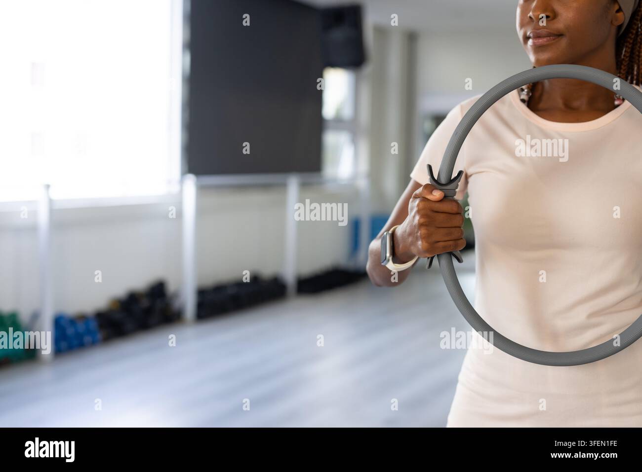 Afrikanische Frau hält grauen Pilatesring, trägt hellrosa Oberteil, Smartwatch im Studio, Kopierraum Stockfoto