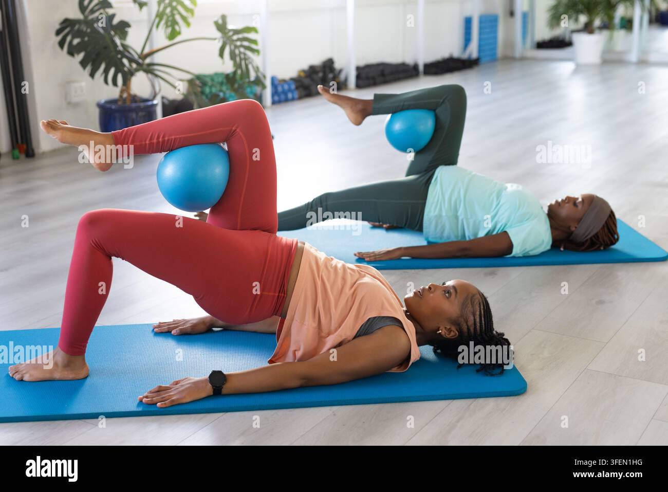 Zwei afrikanische Frauen machen Glute-Bridge auf blauen Matten im Studio in Leggings und halten Fitnessbälle Stockfoto