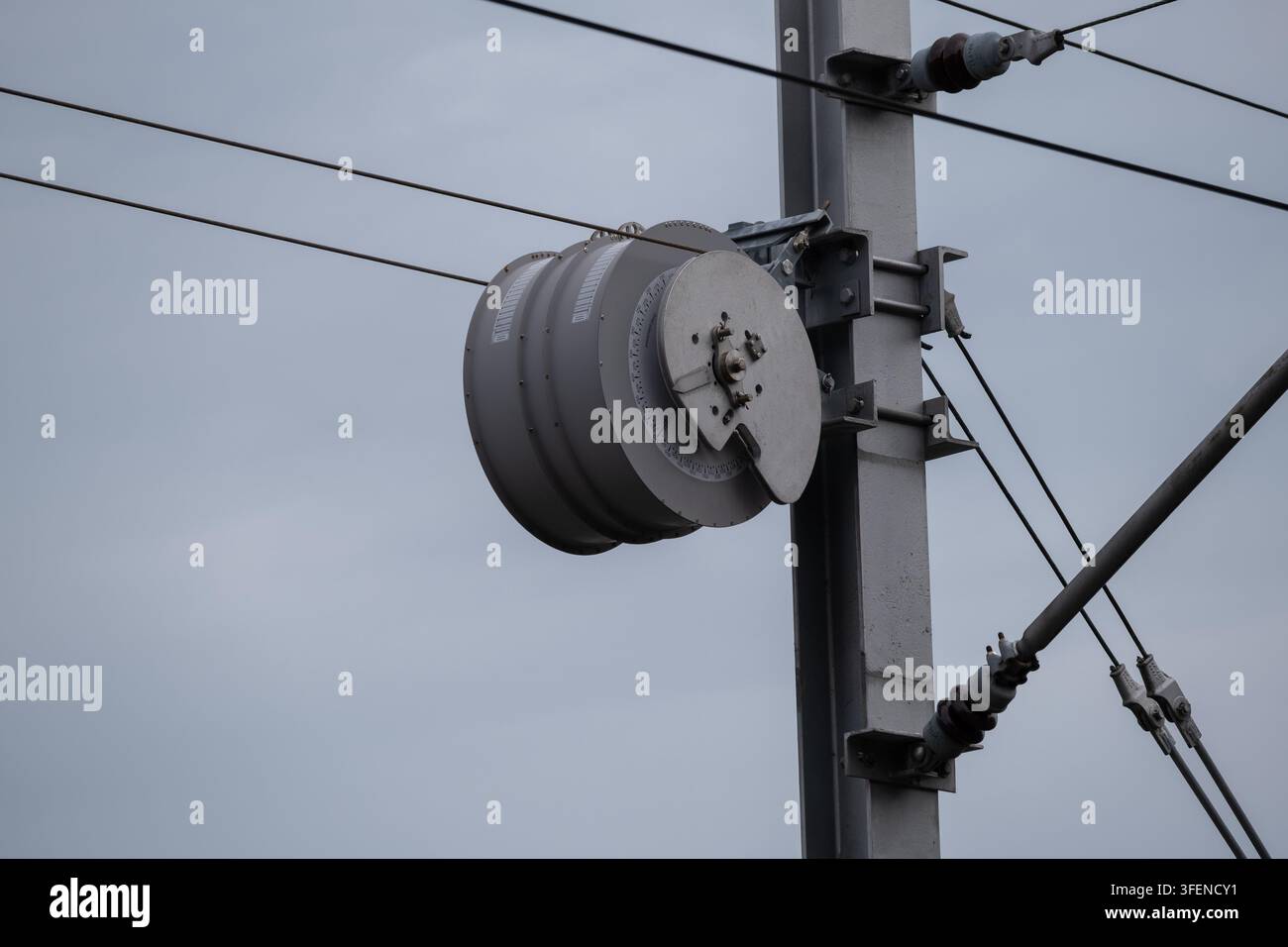 Nahaufnahme von elektrischen Geräten und Isolatoren, die auf einem Strommast montiert sind, mit Überkopfstromleitungen vor einem bewölkten Himmel. Stromverteilung und Stockfoto