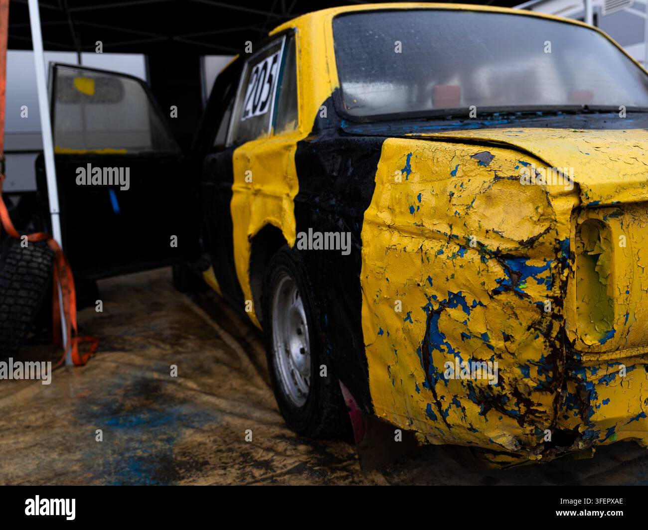 Nahaufnahme eines stark beschädigten gelb-schwarzen Folkrace-Autos mit verbeulten und zerkratzten Karosserieteilen im Paddock. Stockfoto