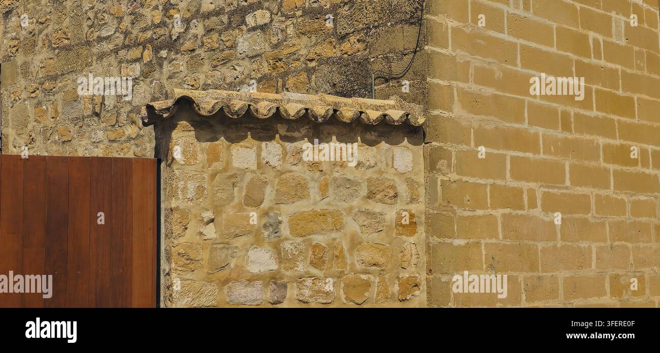 Verwitterte Stein- und Sandsteinmauern mit einer kleinen Lehmziegelbank zeigen kontrastierende traditionelle Texturen in Baeza, Andalusien, Spanien. Stockfoto