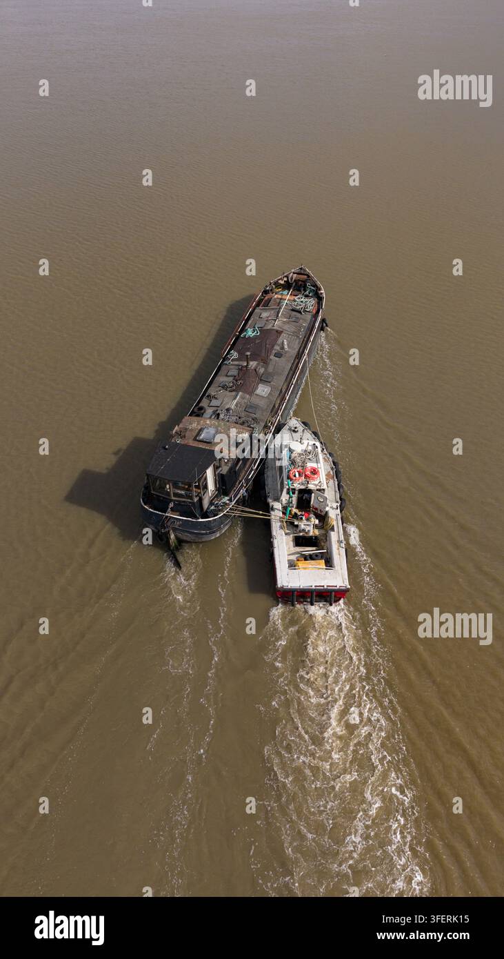 Drohnenluftbild eines Schleppboots, das einen Frachtkahn entlang der Themse in England schiebt, und zeigt den Frachttransport auf Binnengewässern Stockfoto