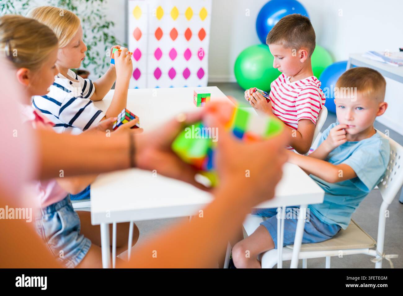 Kinder in einer mentalen Arithmetikstunde üben mit ihrem Lehrer das Lösen von Würfelpuzzles, um Konzentration, Gedächtnis, räumliches Denken und Problemlösungsfähigkeiten zu entwickeln Stockfoto