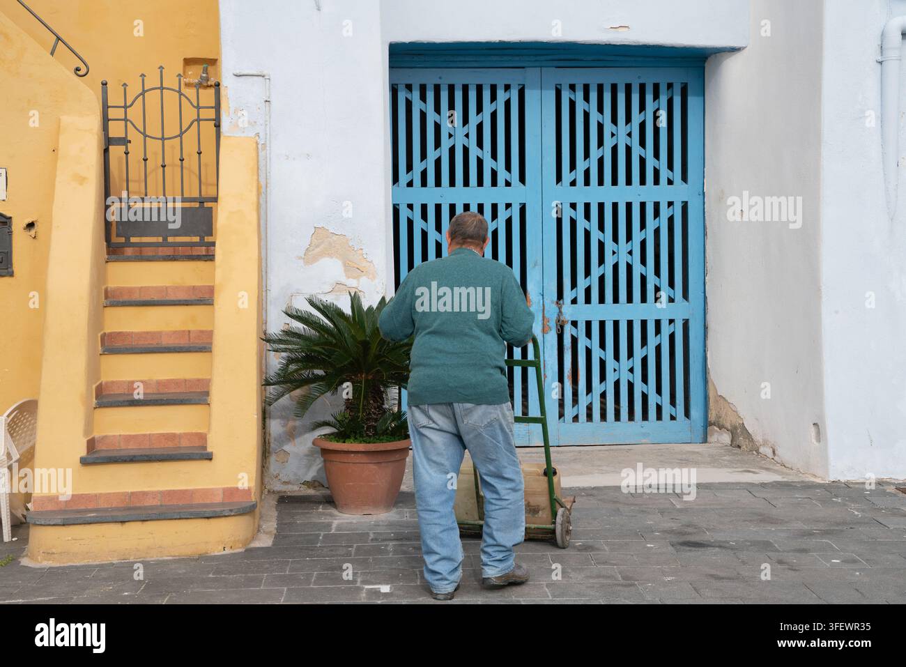 Ein Mann liefert Vorräte mit einem Handwagen in La Marina di Corricella, dem im 17. Jahrhundert erbauten Hafen von Procida, der für seine spontane Architektur berühmt ist. Stockfoto