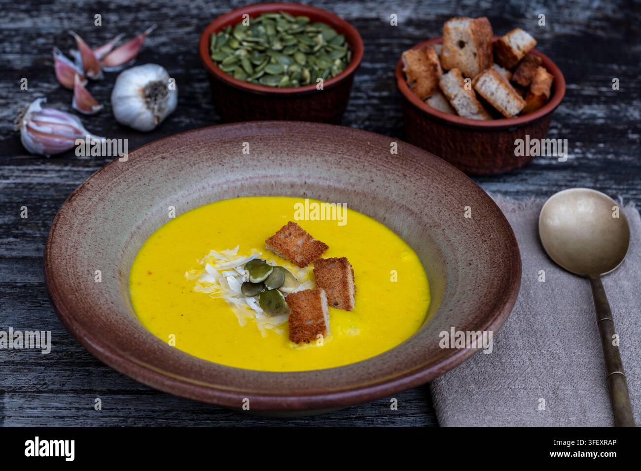 Kürbiskremesuppe mit Croutons und Samen in einer Keramikschüssel. Köstliche gelbe Kürbispüreesuppe serviert mit knusprigen Croutons, Kürbiskernen und Knoblauch Stockfoto
