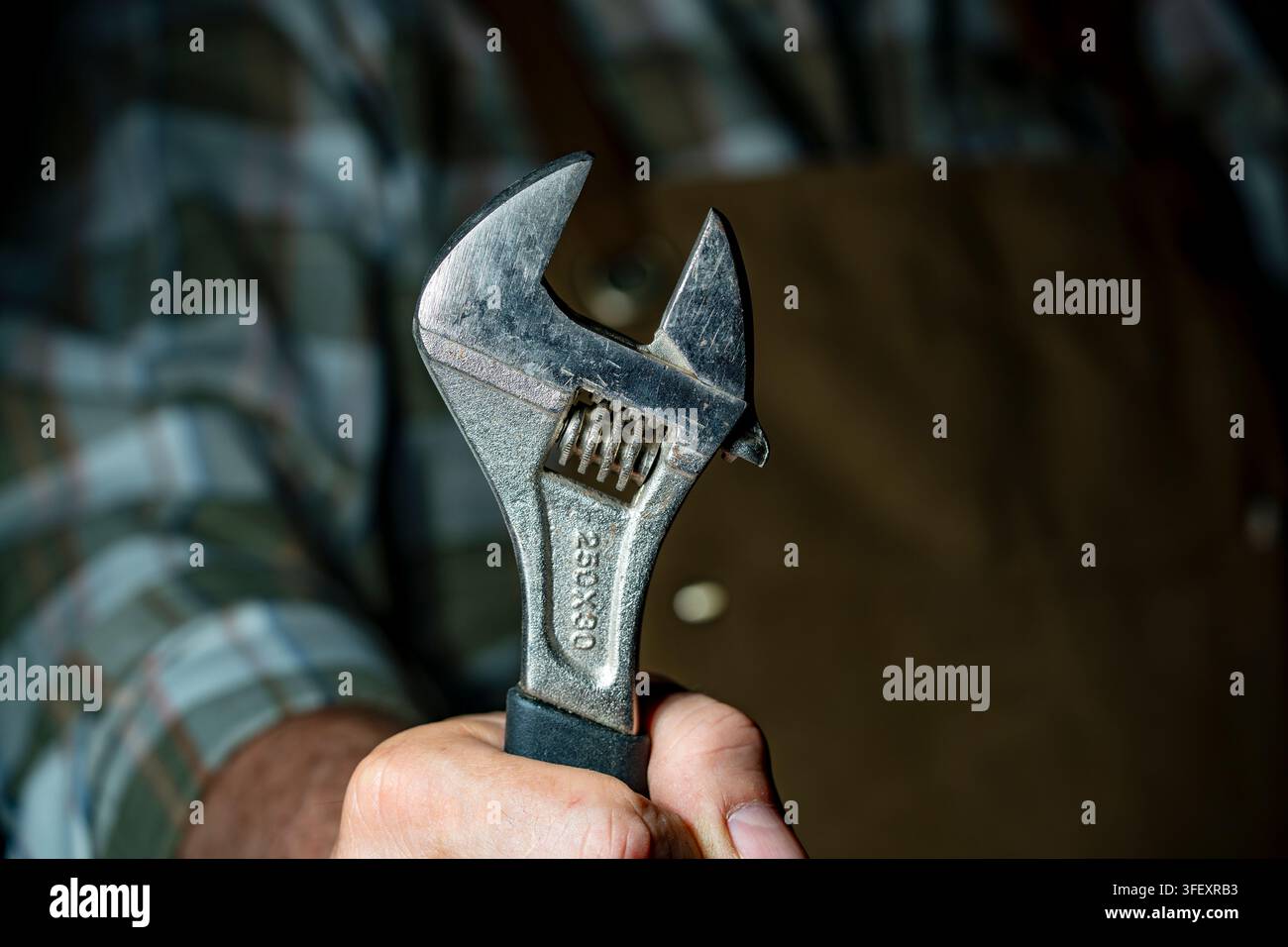 Nahaufnahme einer Hand, die einen schweren verstellbaren Schraubenschlüssel hält. Mechaniker- oder Zimmermannhand, die einen Vintage-Stahlspanner umklammert, Reparaturarbeiter mit industriellem Handwerkzeug Stockfoto