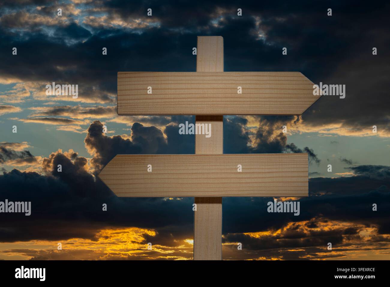 Leeres Holzschild mit Pfeilen, die in entgegengesetzte Richtungen zeigen, bei Sonnenuntergang, Nahaufnahme. Leeres Holzkreuzungsschild, das nach links und rechts zeigt, vor dramatischer Kulisse Stockfoto