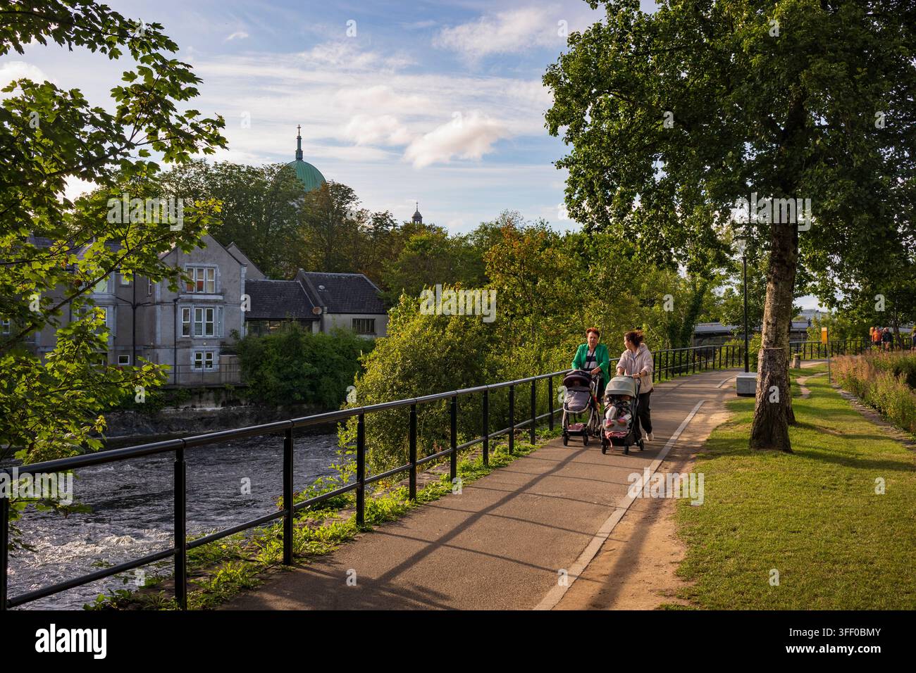 Galway, Irland, 6. Aug. 2026: Eine Gruppe von Menschen spaziert einen Pfad entlang, der den Fluss Corrib in Galway, Irland, umschlingt, spät am Tag nahe Sonnenuntergang in Stockfoto