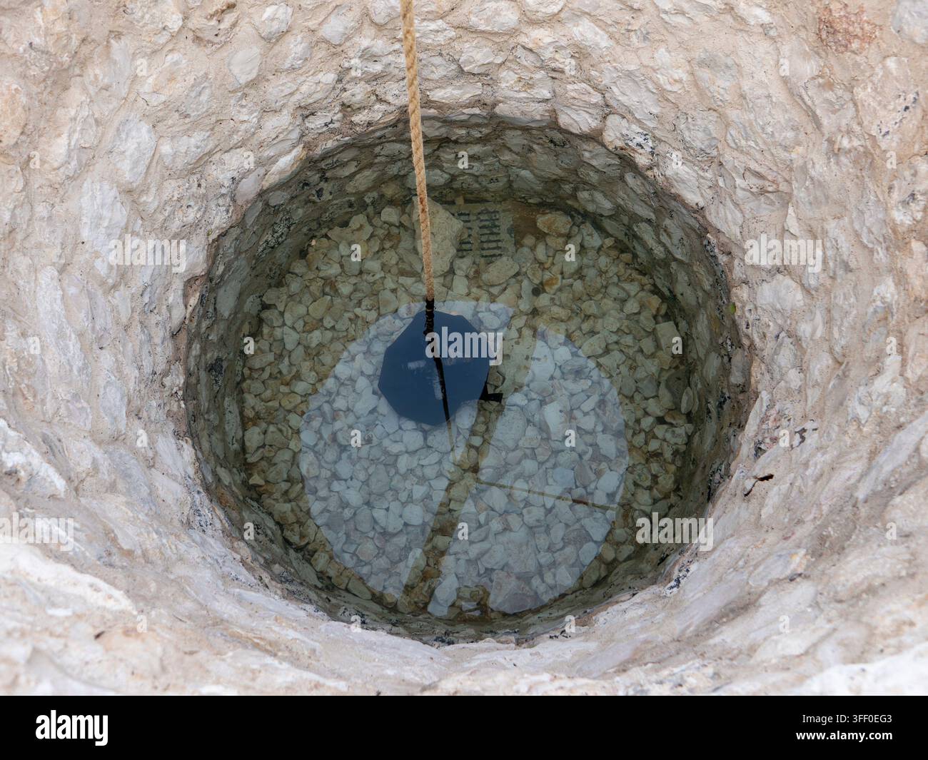 Blick hinab in einen historischen, steinernen Brunnen mit aufgehängtem Seil und Eimer im Innenhof des Nationalmuseums von Katar. Stockfoto