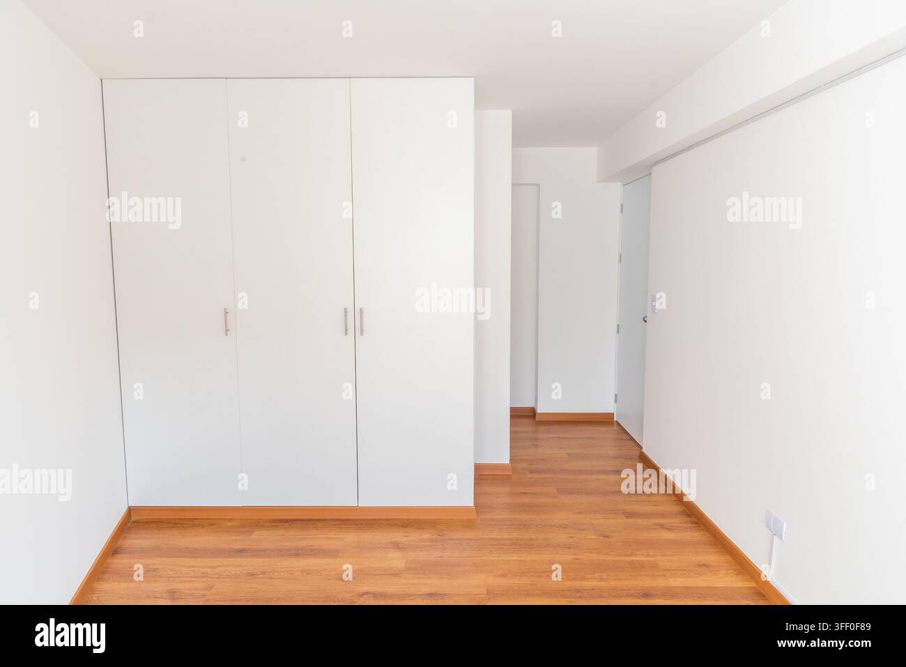 Minimalistisches Interieur: Ein leerer Raum mit einem großen weißen Kleiderschrank und Holzboden, der einen sauberen und aufgeräumten Lebensraum präsentiert. Stockfoto