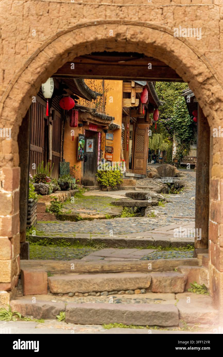 Steinerne Torbogen, der eine laternenbeleuchtete Straßenansicht einrahmt, Shaxi Altstadt, Yunnan, China Stockfoto