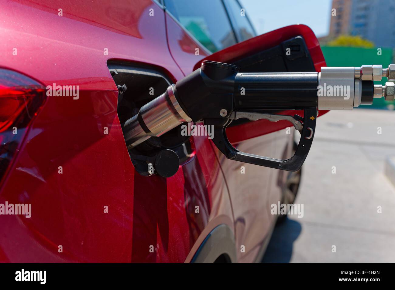 Rotes Auto tankt an einer Tankstelle, zeigt eine Nahaufnahme der Pumpendüse in der Tanköffnung Stockfoto