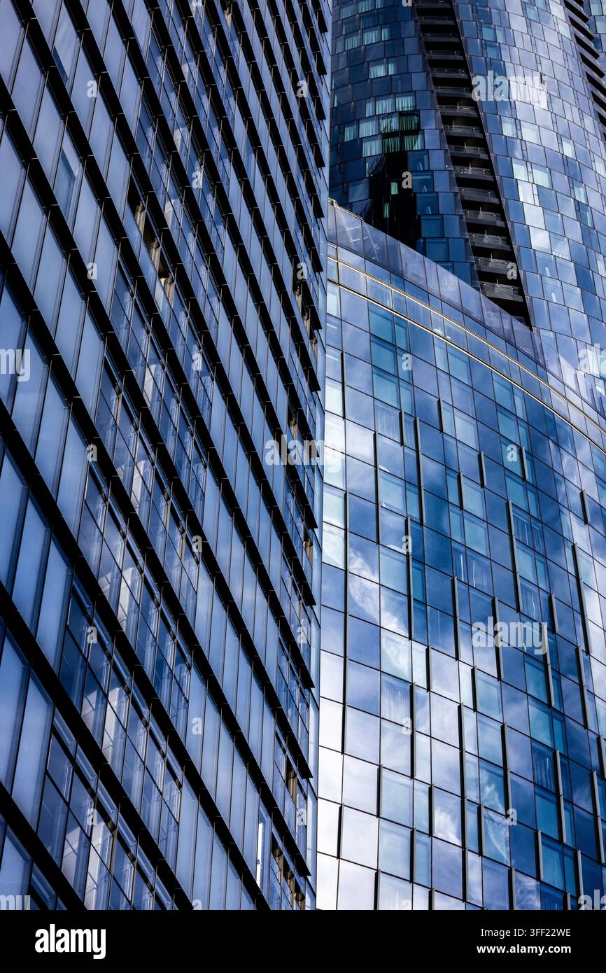 Gläserne Bürotürme spiegeln Himmel und Wolken wider, ihre rasterartigen Fenster Muster erzeugen kontrastierende Winkel und Tiefen. Stockfoto