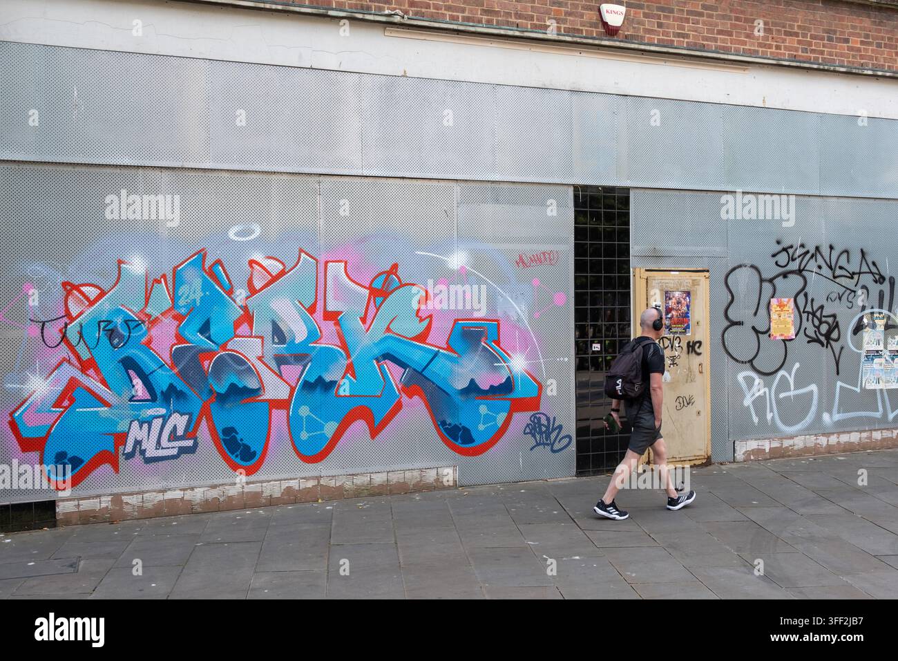 Person, die an verrammelten Läden mit graffitikoverten Rolltoren in der Arundel Street, Portsmouth, England, UK vorbeigeht Stockfoto