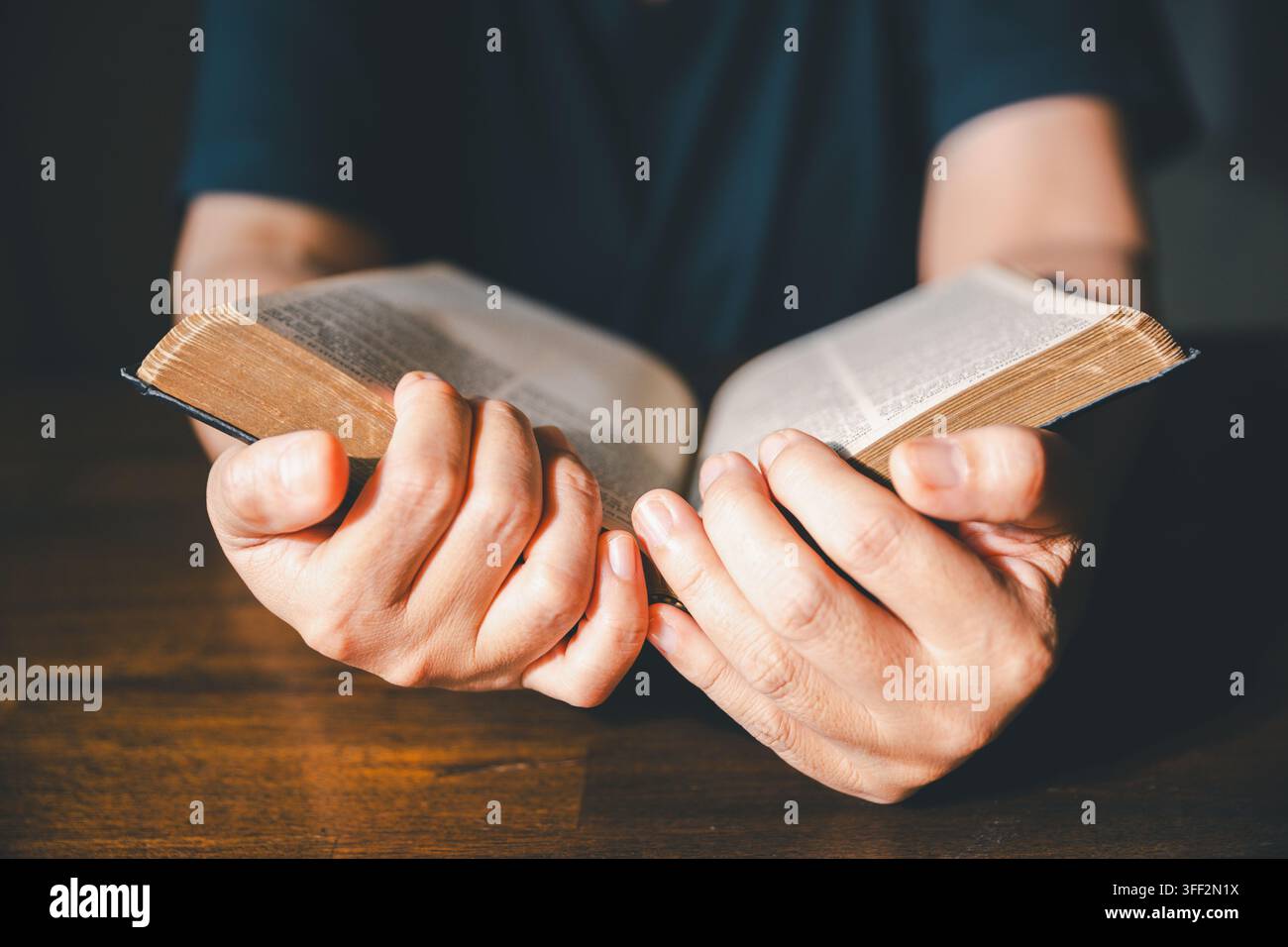 Nahaufnahme von Händen, die die Seiten einer alten Bibel auf einem Holztisch umblättern, was das Lesen christlicher Schriften, das Glaubensstudium, die Hingabe, die Anbetung und das Spirituelle darstellt Stockfoto