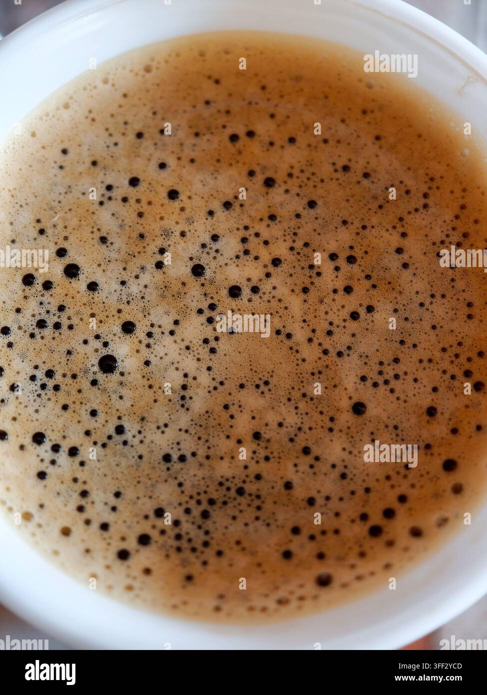 Kaffeetasse von oben betrachtet, die den reichen, schaumigen Crema mit zahlreichen kleinen dunklen Blasen zeigt, und die verlockende Textur und Wärme des i hervorhebt Stockfoto
