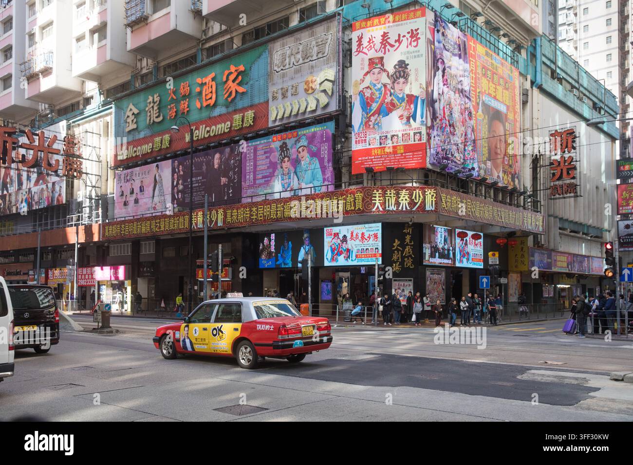 Fußgänger warten vor dem New Light Theatre von North Point in Hongkong, um die Straße zu überqueren, während ein Taxi unter farbenfrohen Show-Plakaten vorbeifährt. Stockfoto