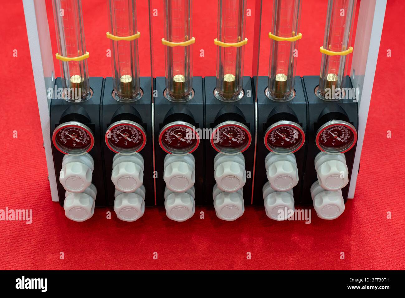 Nahaufnahme eines mehrkanaligen industriellen Ölschmiersystems mit transparenten Reservoirs, Temperaturanzeigern und Durchflussregelventilen Stockfoto