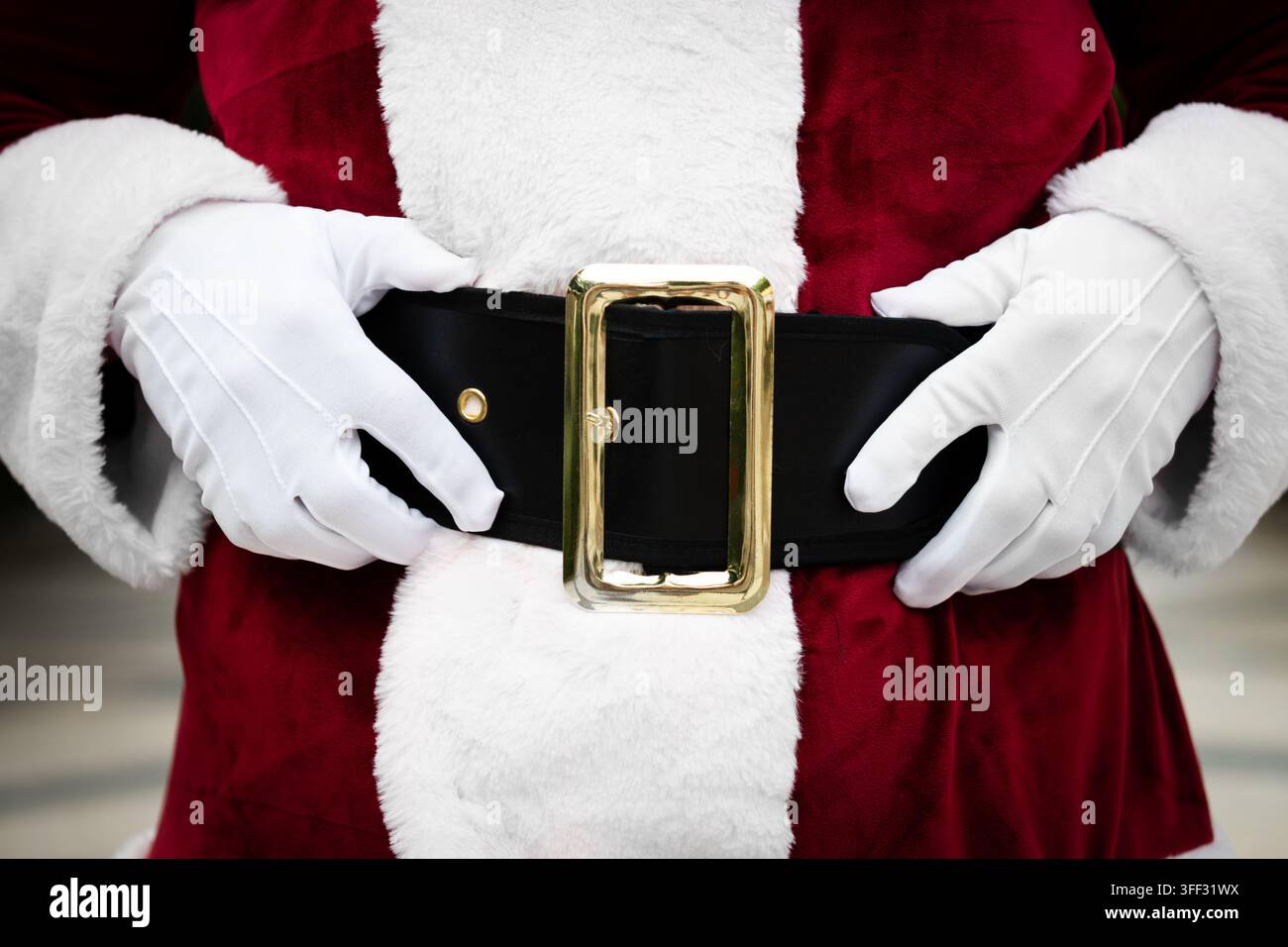 Detaillierte Nahaufnahme eines Weihnachtsmann-Kostüms, das einen traditionellen schwarzen Gürtel mit goldener Schnalle, weiße Handschuhe und einen roten Weihnachtsanzug zeigt. Stockfoto